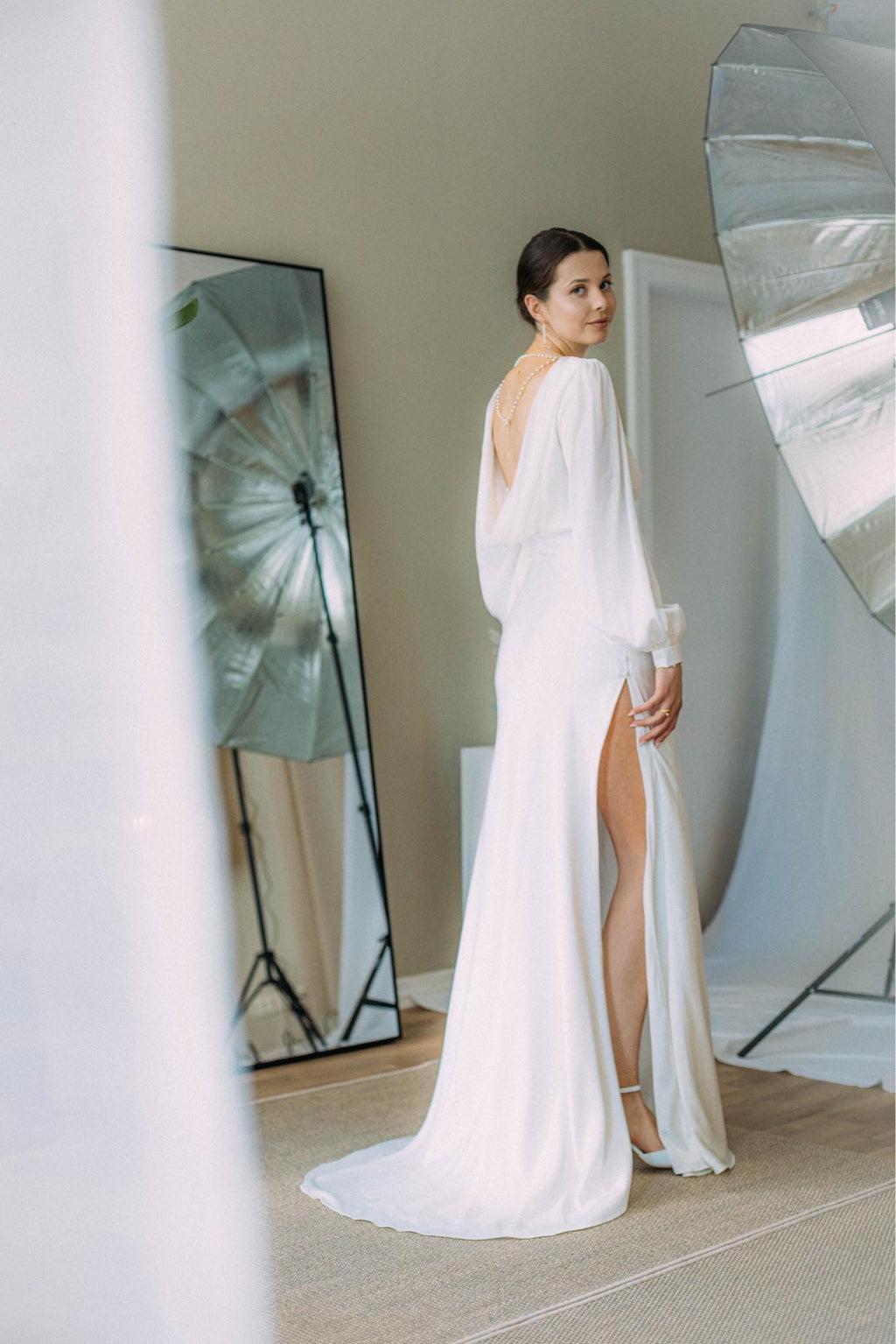 Elegante Braut in Satin-Hochzeitskleid mit langen Bischofsärmeln, offenem Rücken und seitlichem Schlitz im Rock, Brautmode Hamburg