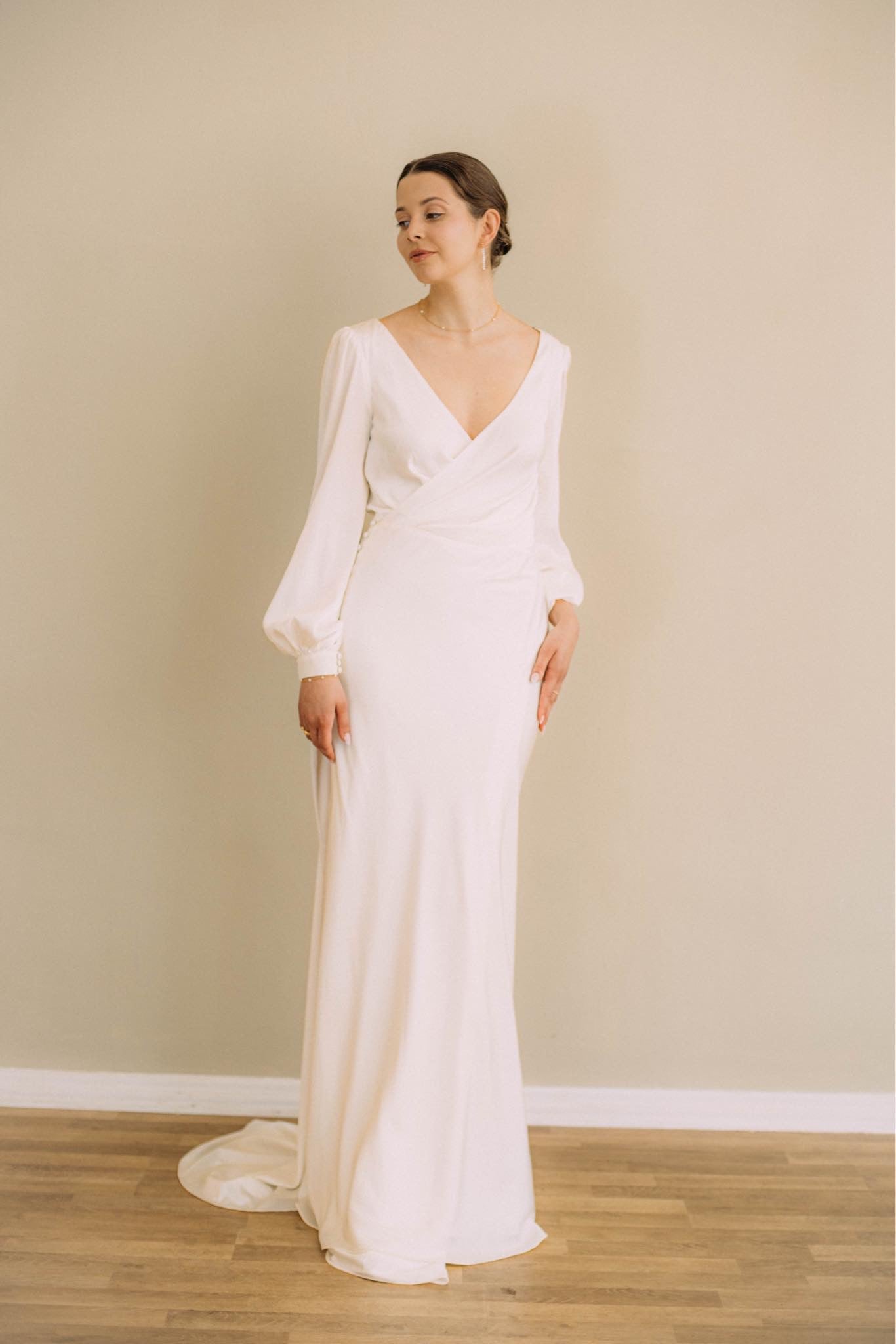 Elegante Braut in Satin-Hochzeitskleid mit langen Bischofsärmeln, offenem Rücken und seitlichem Schlitz im Rock, Brautmode Hamburg