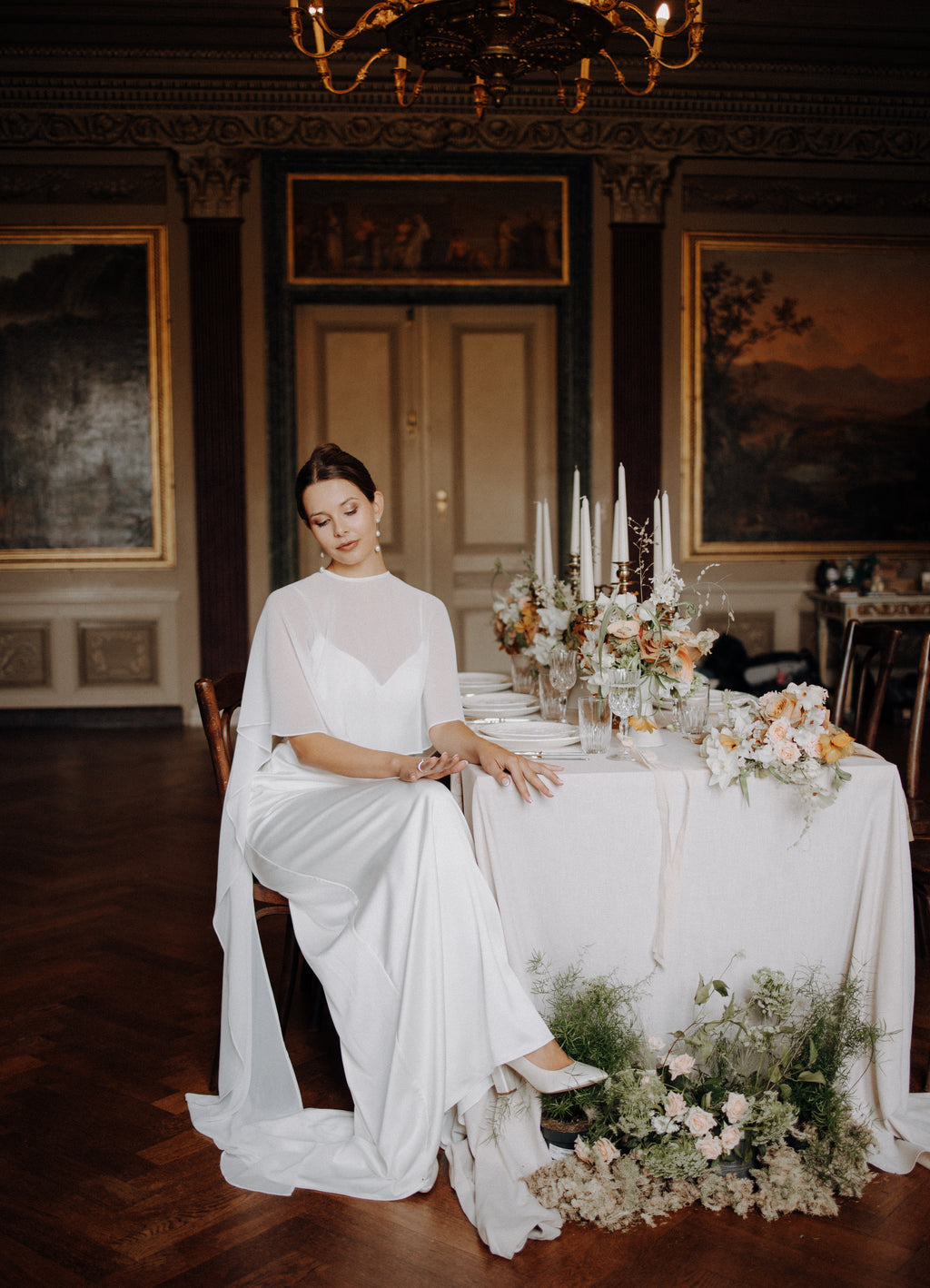 Sheer white chiffon wedding cape flowing softly over the shoulders, adding a delicate and ethereal touch to the bridal look Zarter, transparenter Chiffon-Brautcape in Weiß, der sanft über die Schultern fällt und dem Brautlook eine elegante, ätherische Note verleiht.