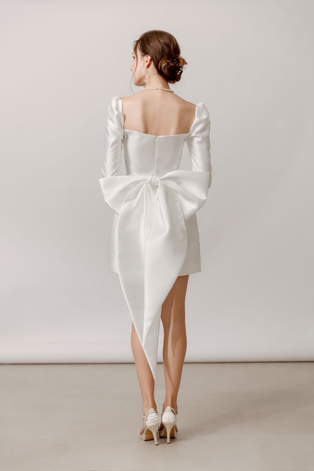 Elegante Braut in Mini-Hochzeitskleid mit langen Ärmeln und Schleife am Rücken, Hamburg.