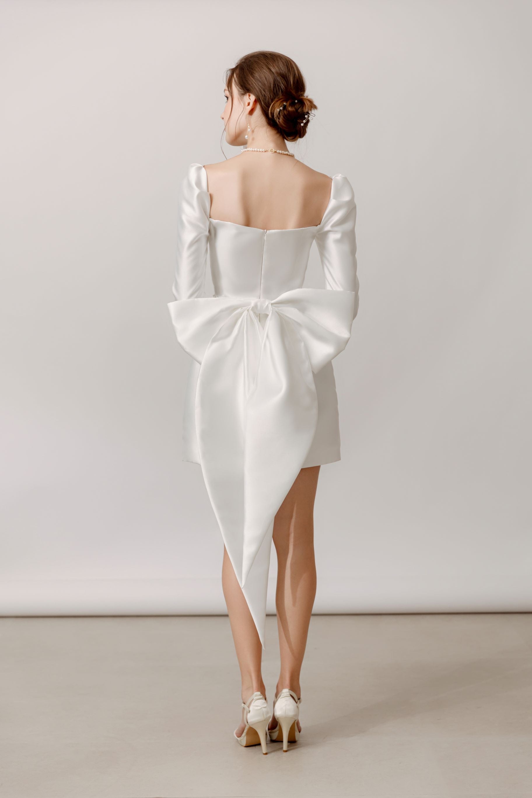 Elegante Braut in Mini-Hochzeitskleid mit langen Ärmeln und Schleife am Rücken, Hamburg.