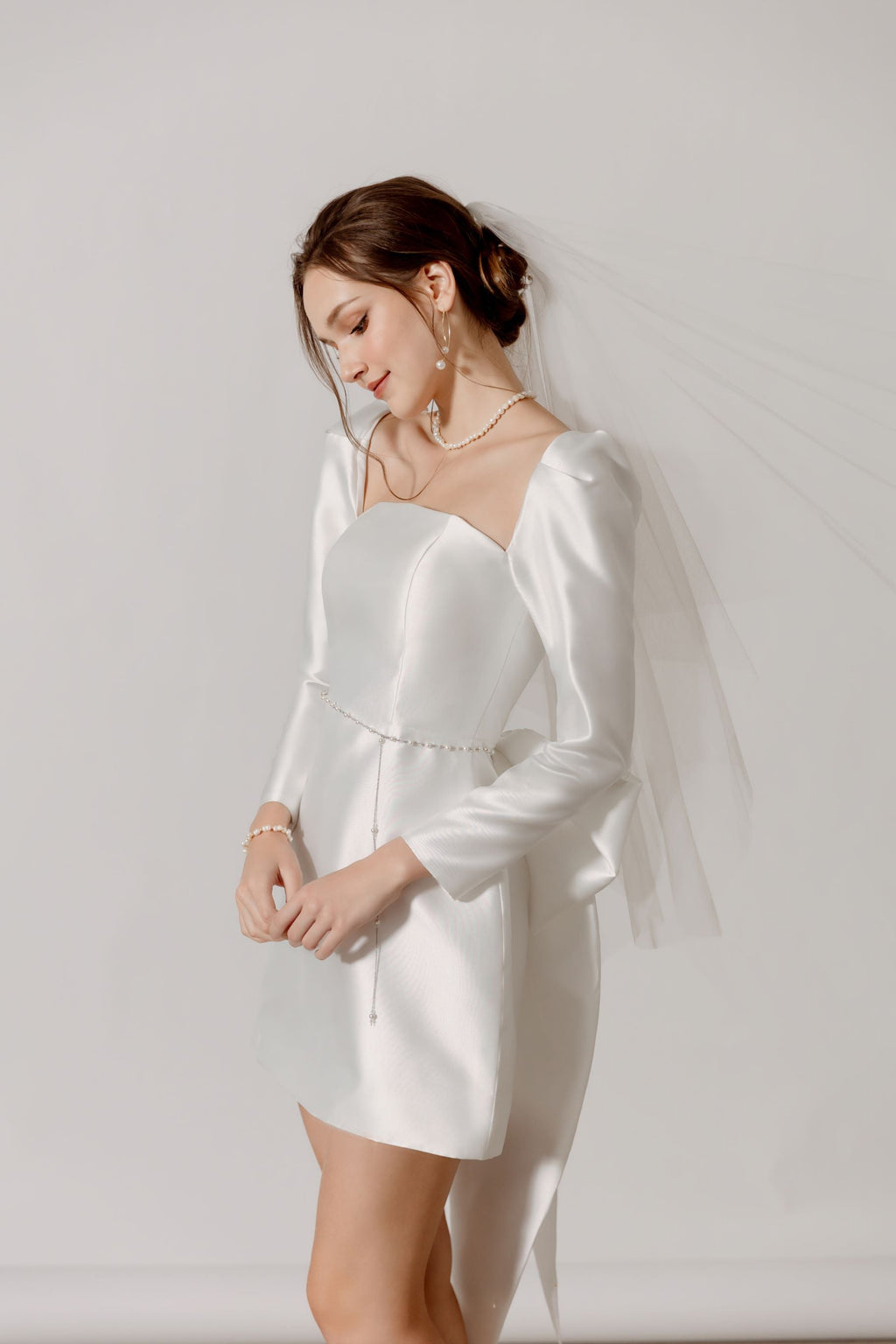 Elegante Braut in Mini-Hochzeitskleid mit langen Ärmeln und Schleife am Rücken, Hamburg.