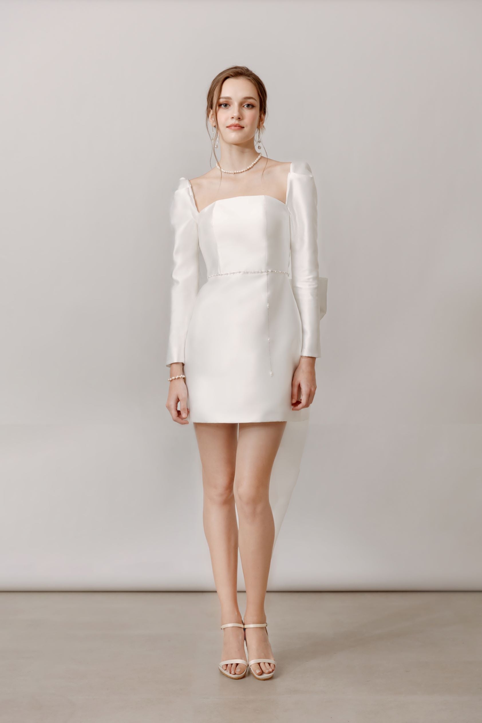 Elegante Braut in Mini-Hochzeitskleid mit langen Ärmeln und Schleife am Rücken, Hamburg.